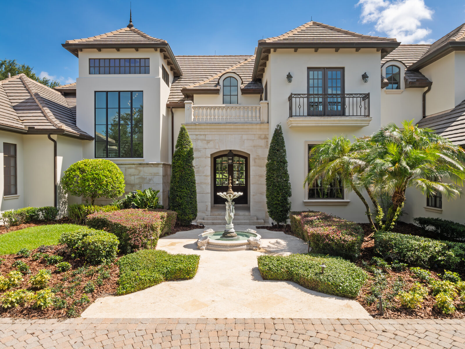 Daytime front elevation of the fully renovated Isleworth estate at 9921 Lake Louise Drive with a fountain courtyard