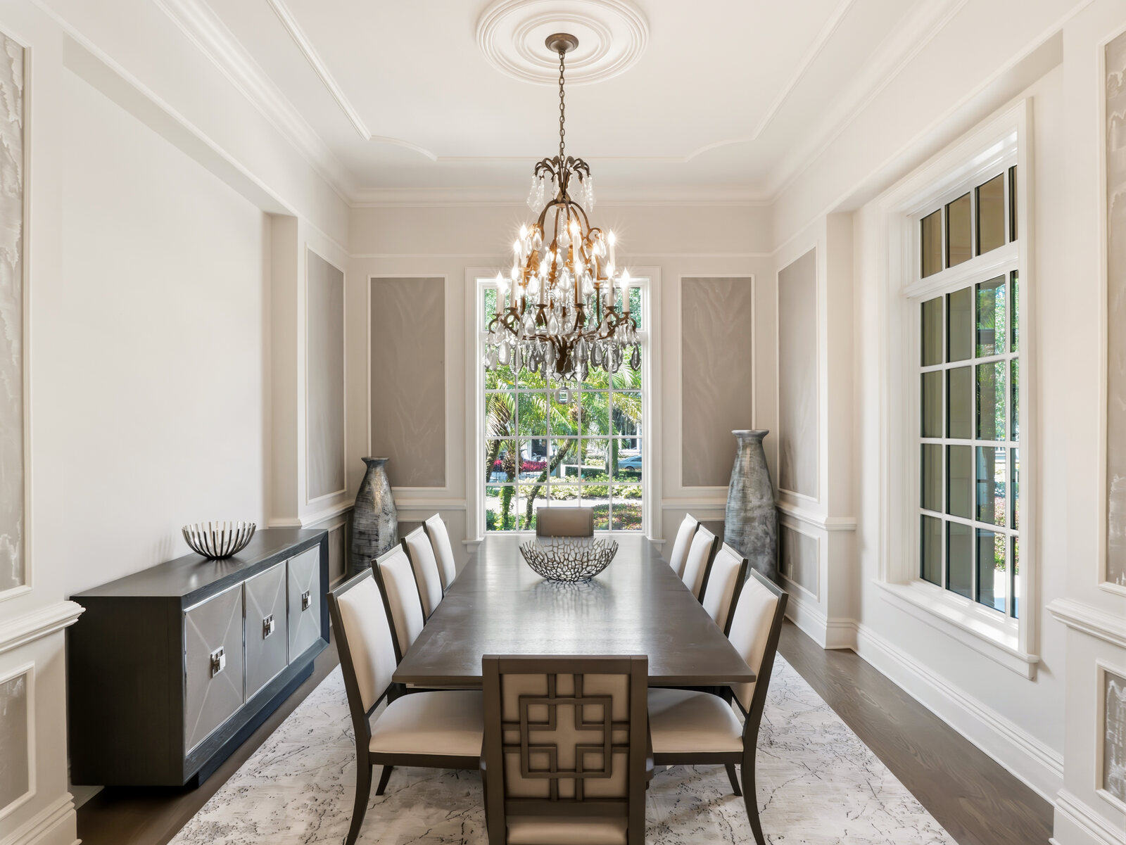 Formal dining room with crystal chandelier and floor-to-ceiling windows overlooking the grounds