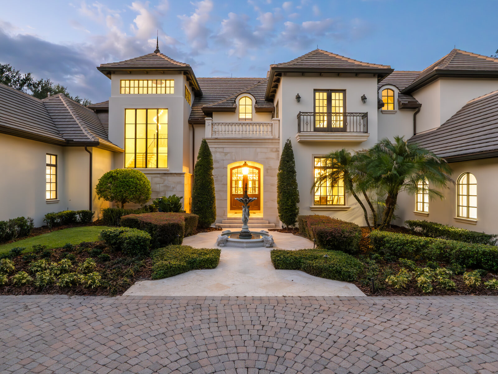 Front elevation of the Isleworth estate at dusk with warm lighting and a fountain courtyard