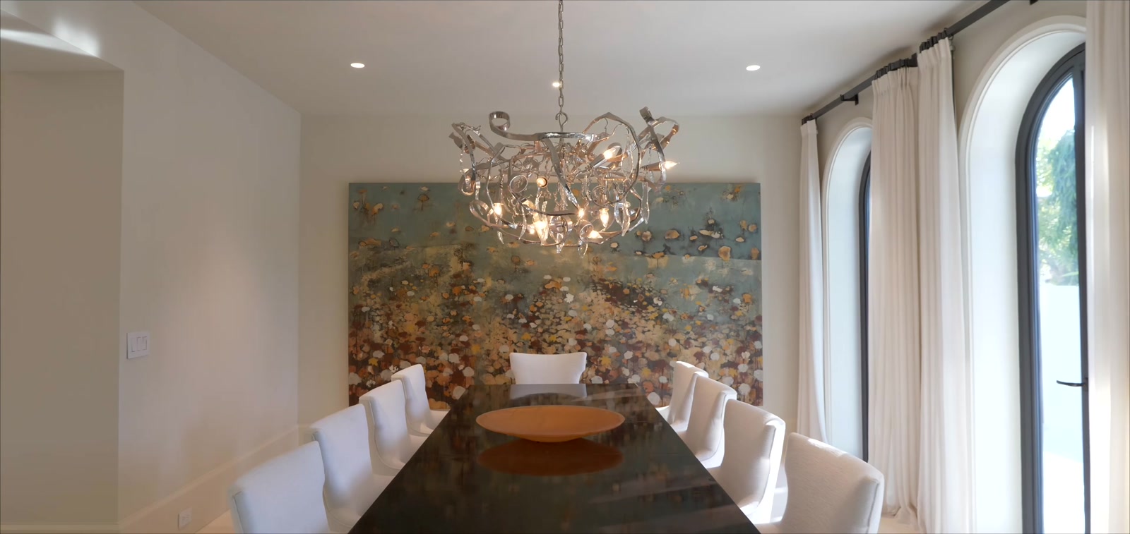 Formal dining room with a sculptural chandelier, statement artwork and arched floor-to-ceiling windows