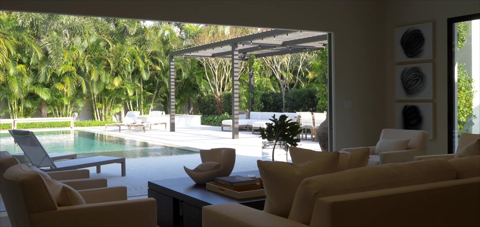 Living room opening through walls of glass to a resort pool and palm gardens at a Snell Isle estate